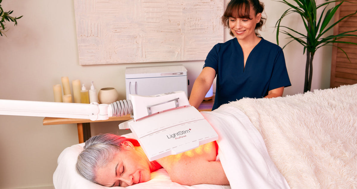 Esthetician providing a LightStim ProPanel treatment on the knee while providing a hand massage.